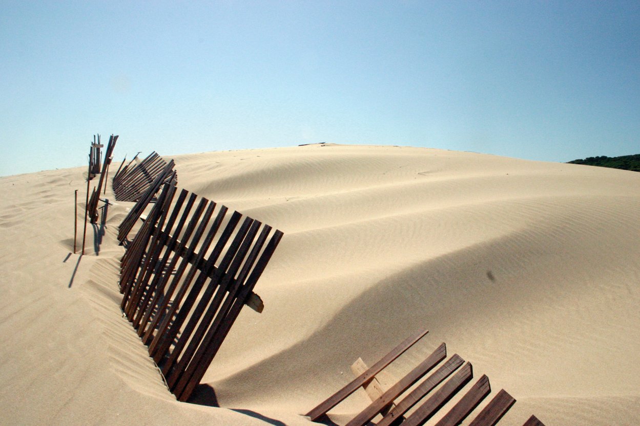 a fence made of wood in the middle of sand dunes