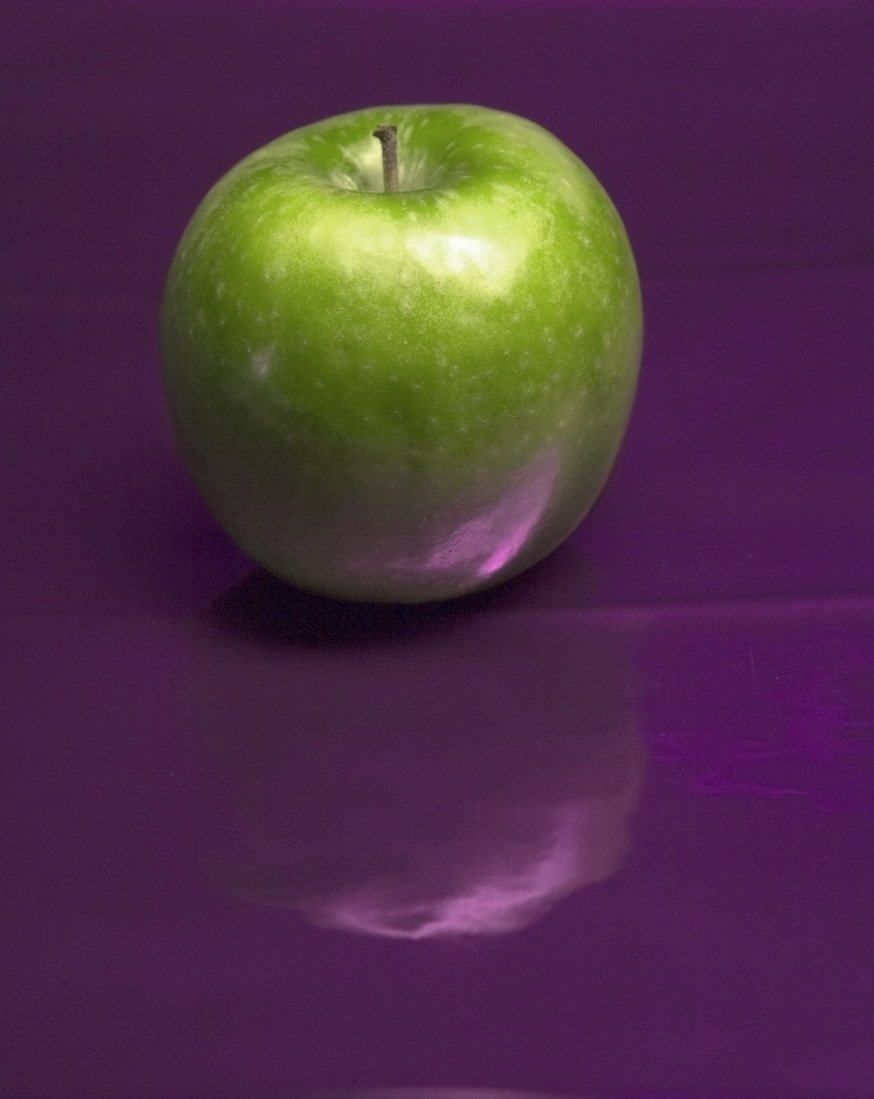 an apple on a shiny surface with a purple light