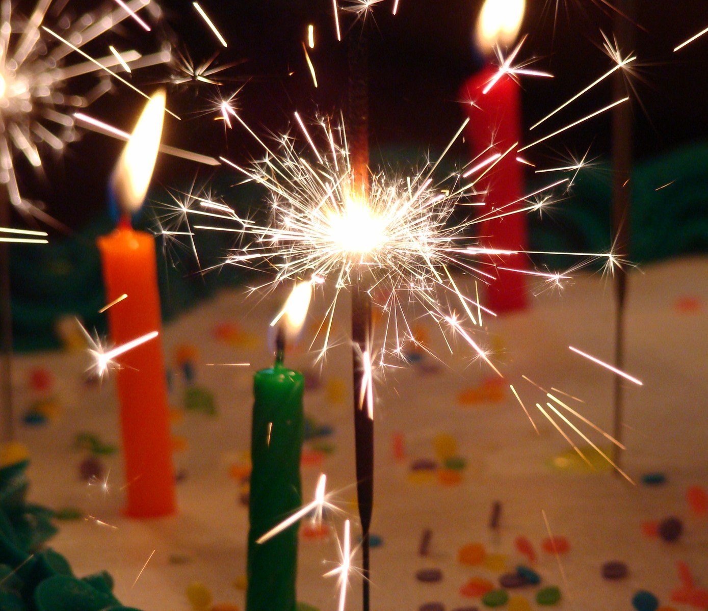 closeup of a birthday cake with multiple candles and one sparkler