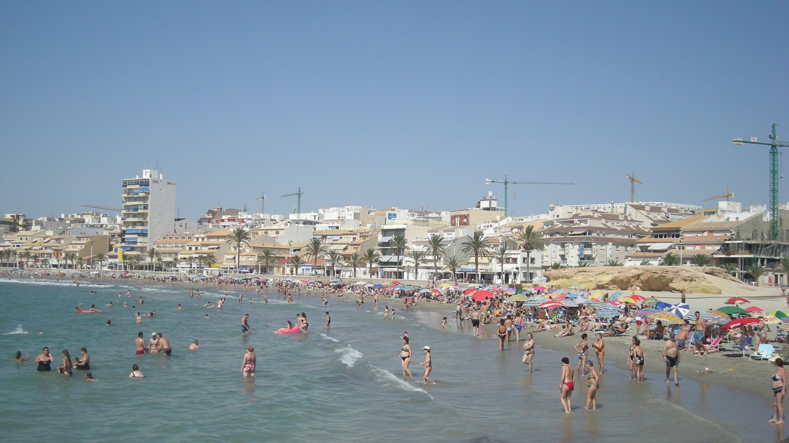 a group of people on a beach with umbrellas and buildings