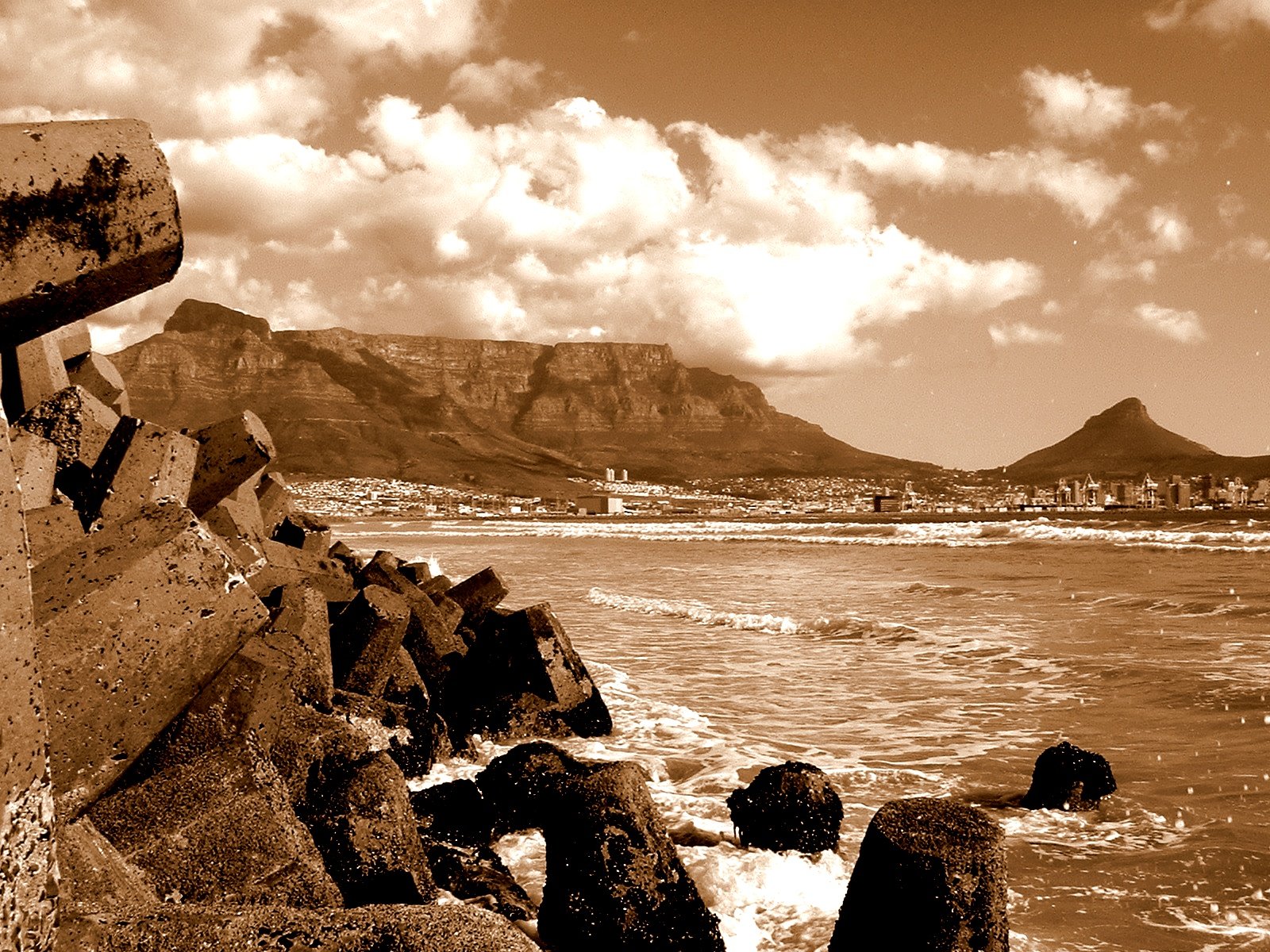 old pograph of rocks on the coast with mountains in the background