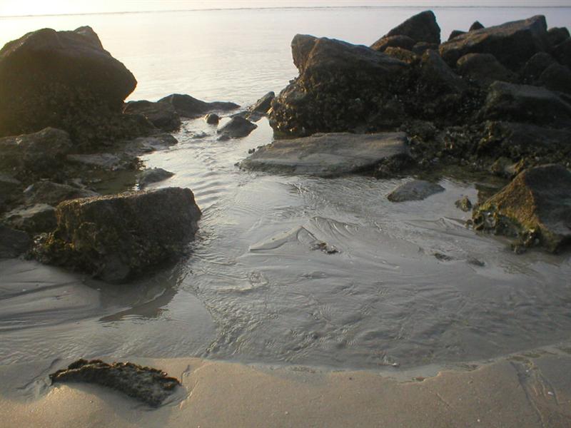 small stream through the beach water, with rocks in the distance