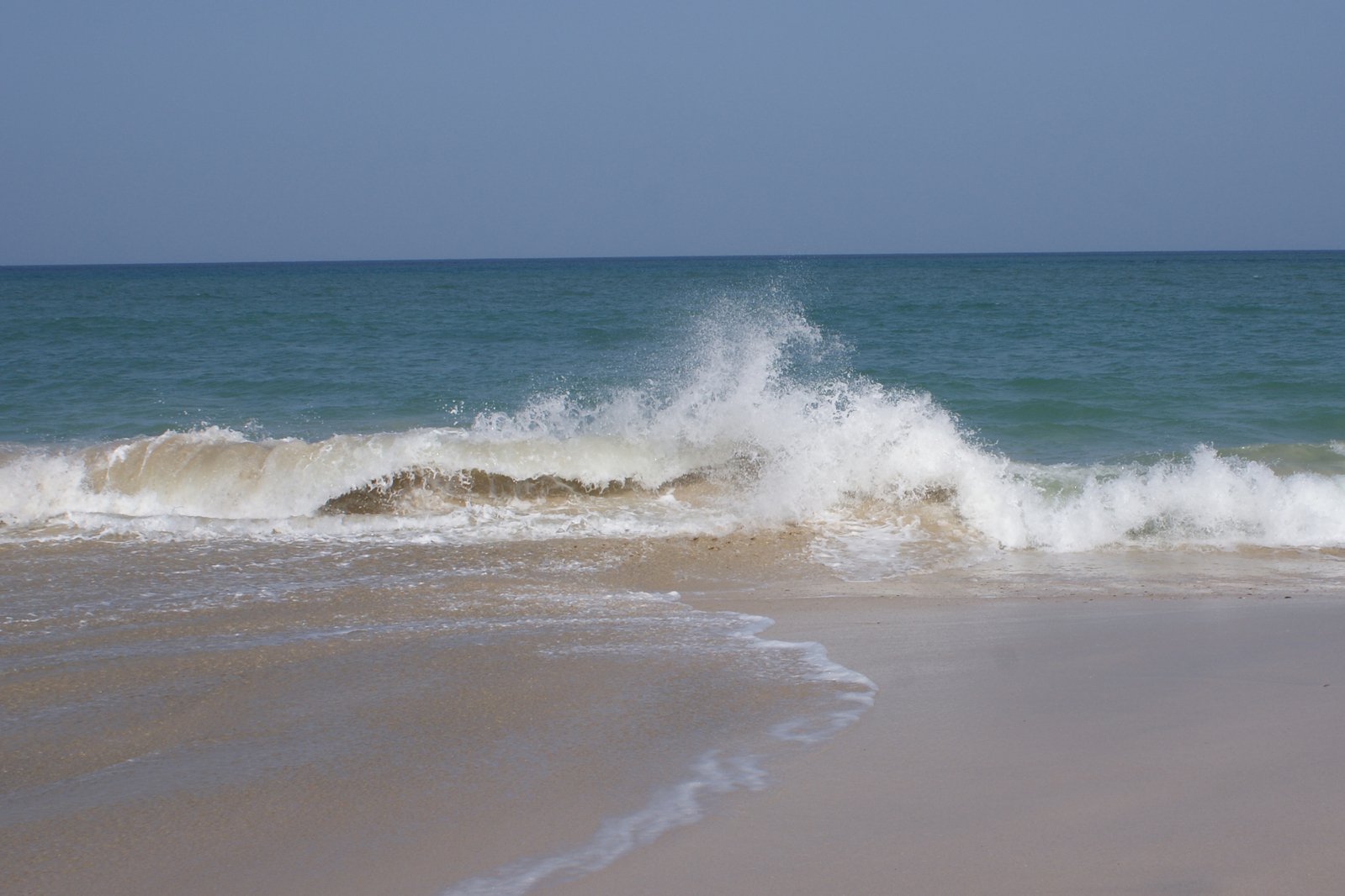 a large white wave rolling into the shore of a beach