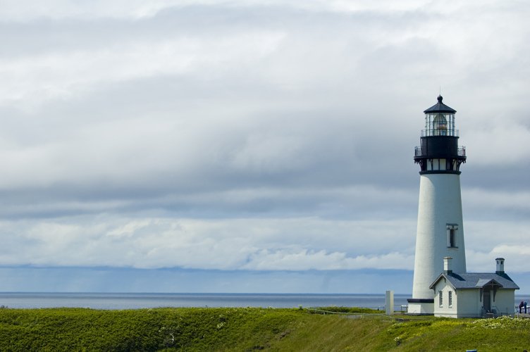 a black and white lighthouse on top of a grassy hill