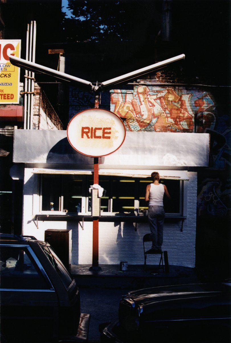 man waiting outside of rice restaurant by some cars