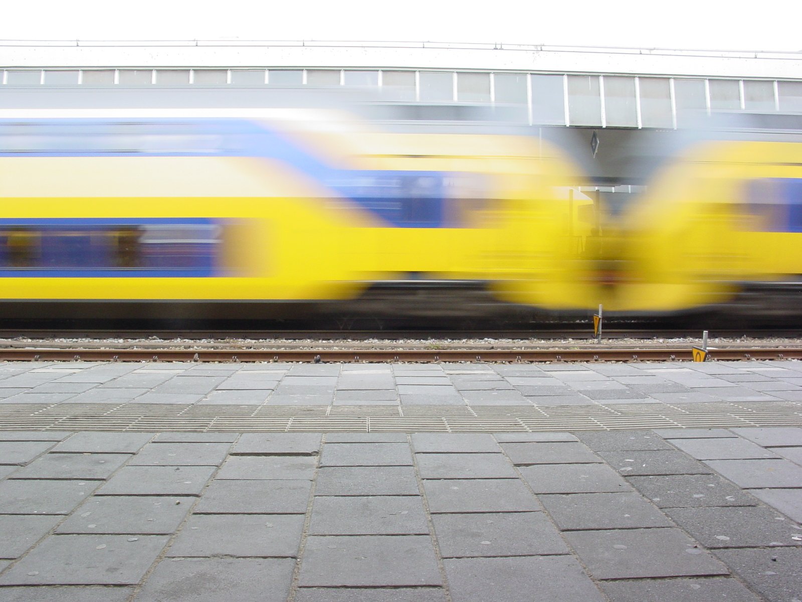 a blue and yellow train speeding by some bricked road