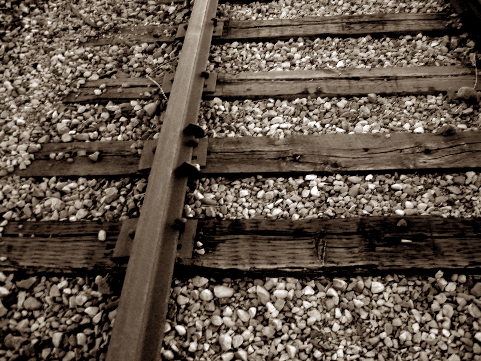 a sepia po of train tracks with pebbles on the bottom and a worn out end