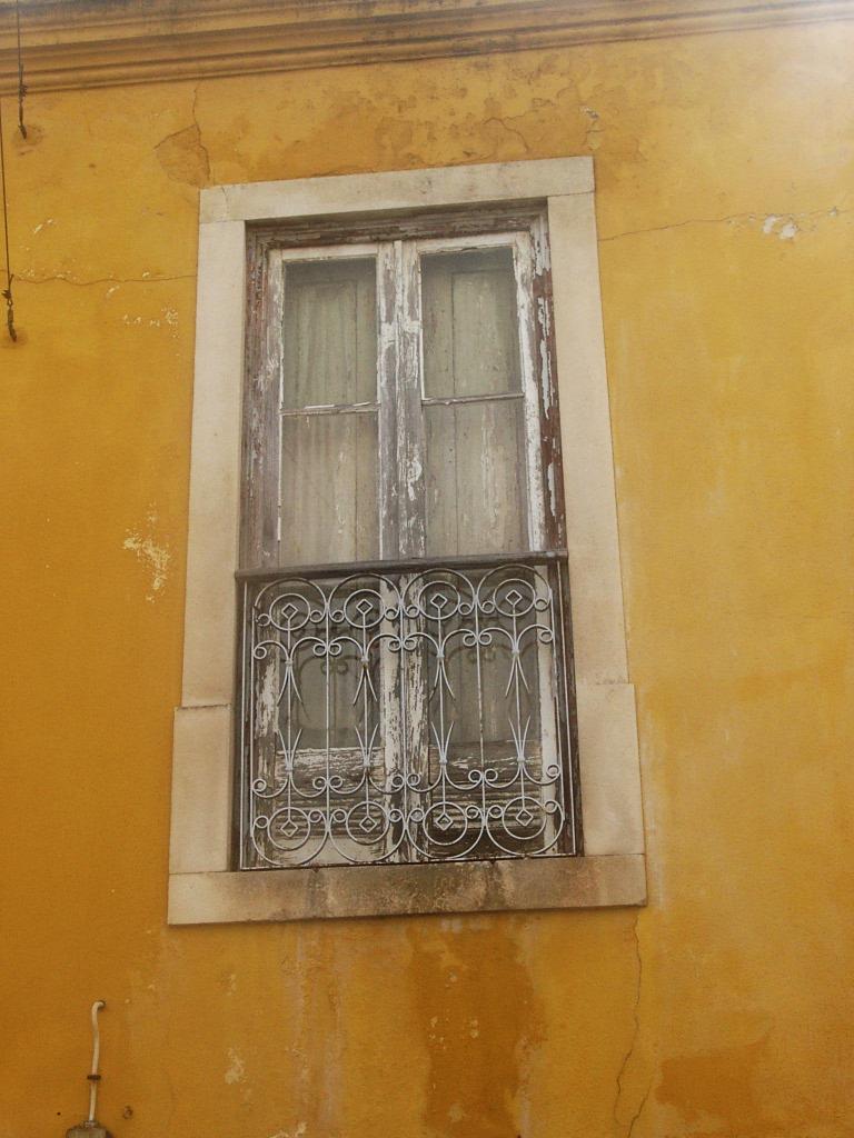 a yellow building with a window and an iron screen on the outside