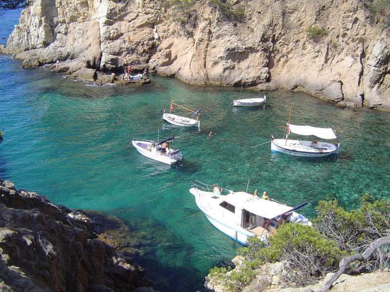 three boats floating in the blue water next to the mountains