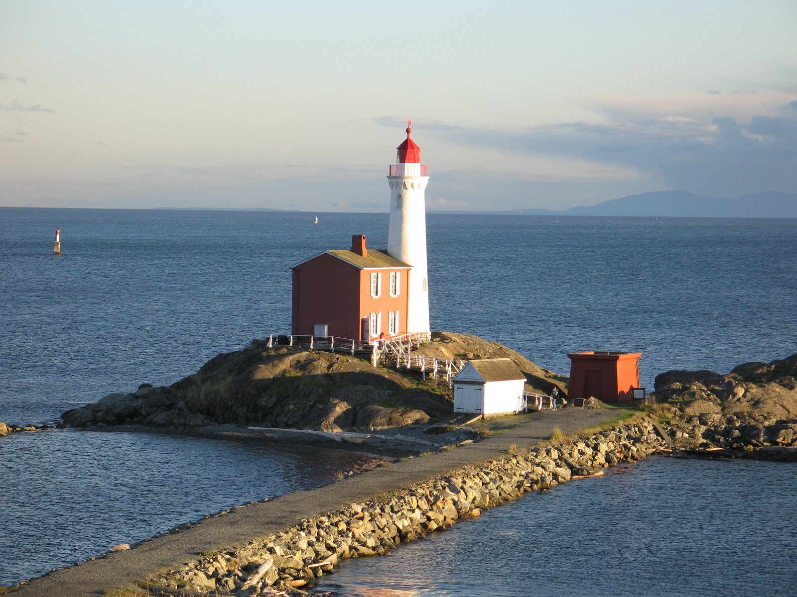 a lighthouse stands on an island with a body of water and sailboats