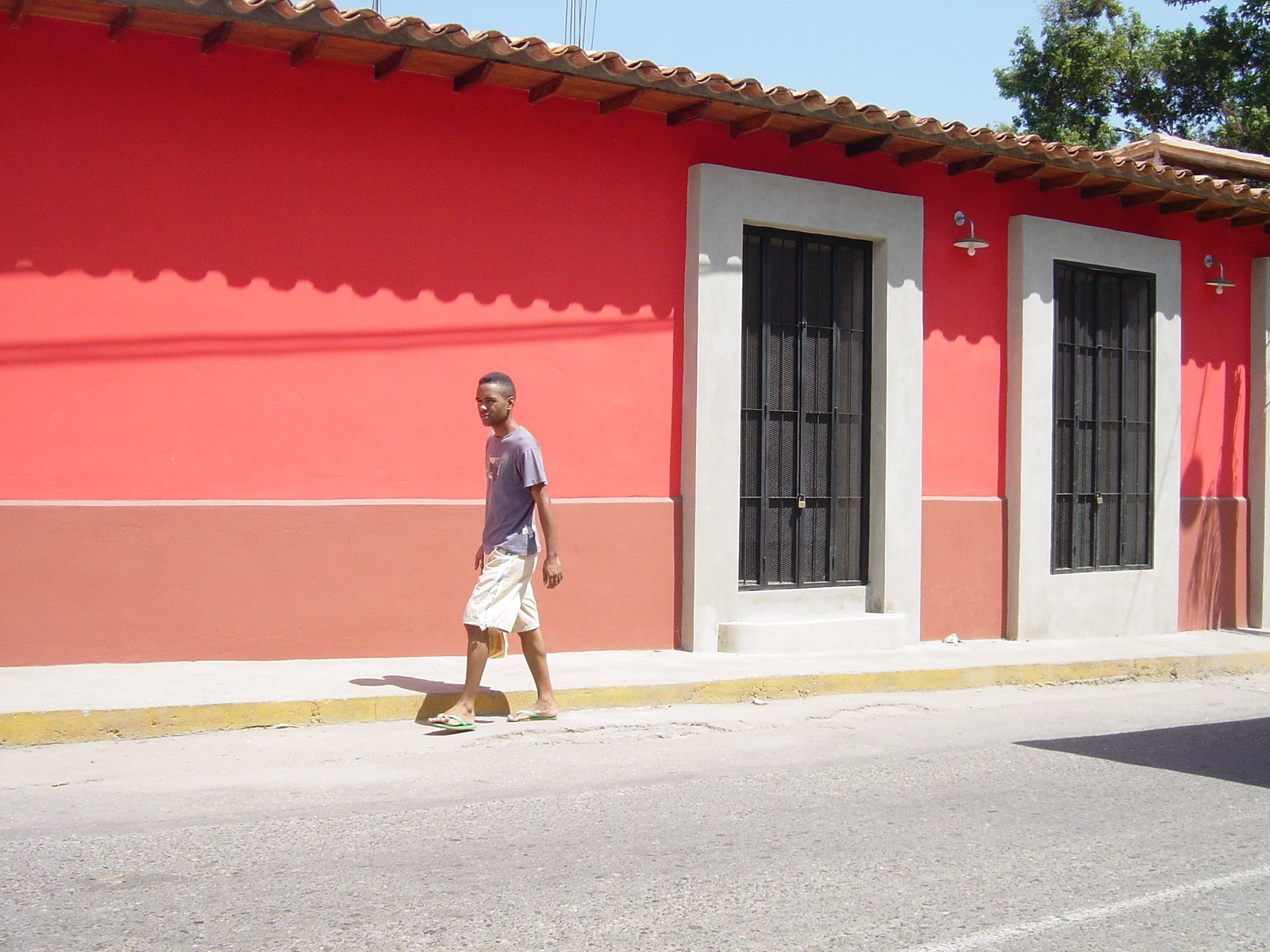 a man is walking on the sidewalk beside an old red and pink building
