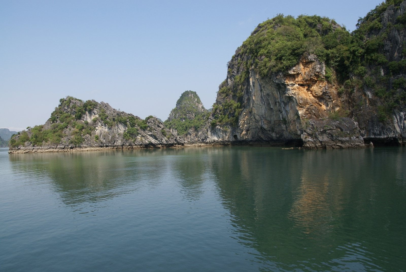 the green mountains on top of a rocky cliff are reflected in the blue water