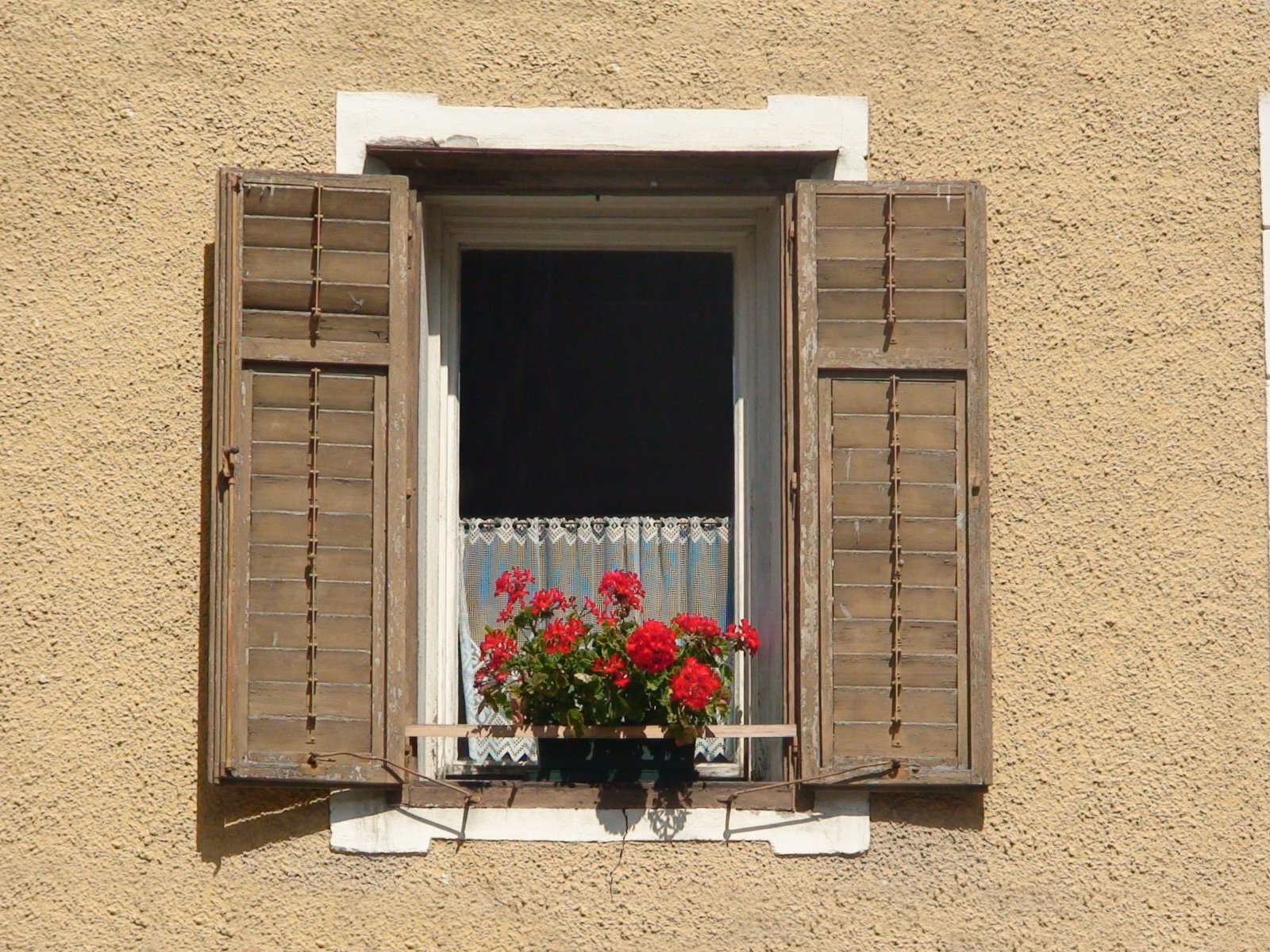 window with open shutters and planter on top of it