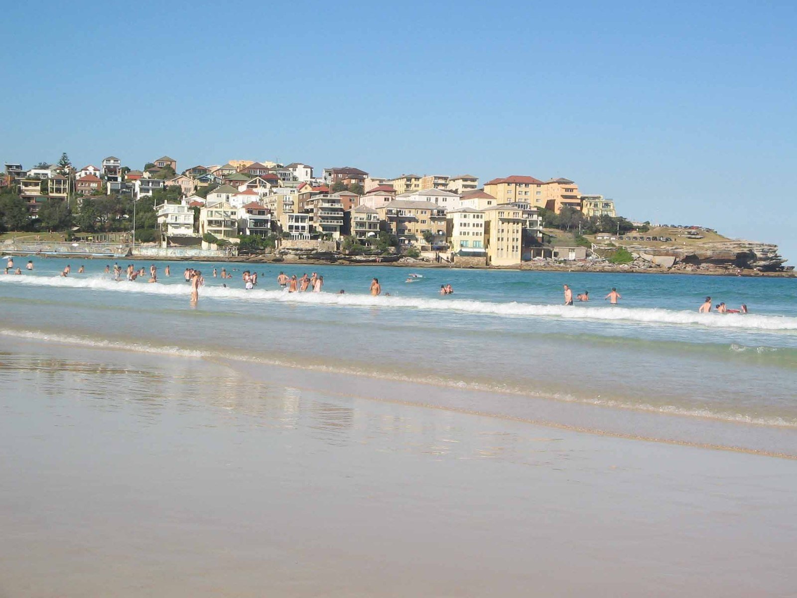 people on the beach near the water with buildings