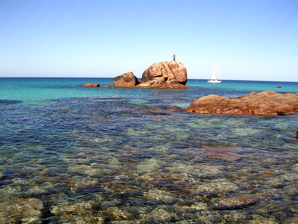 clear blue water surrounding a rocky shore with sail boats