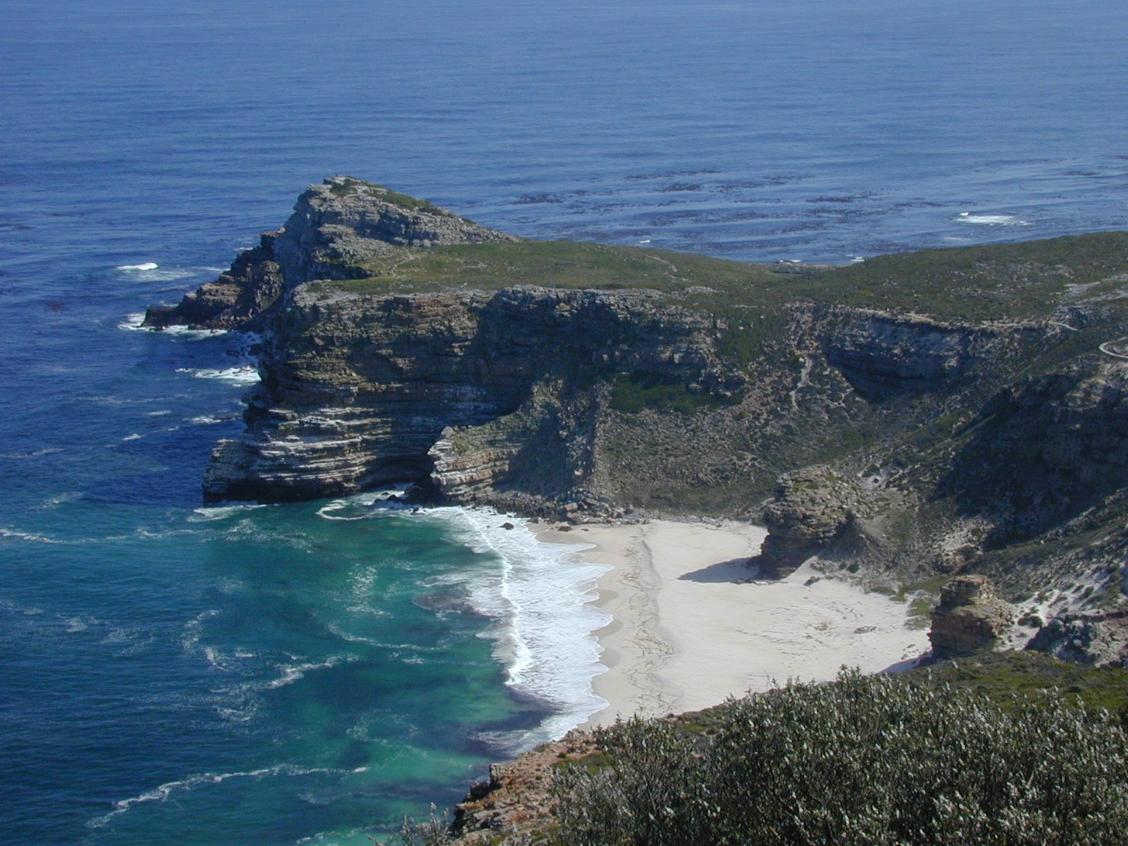 a rocky coast with waves and green grass on it