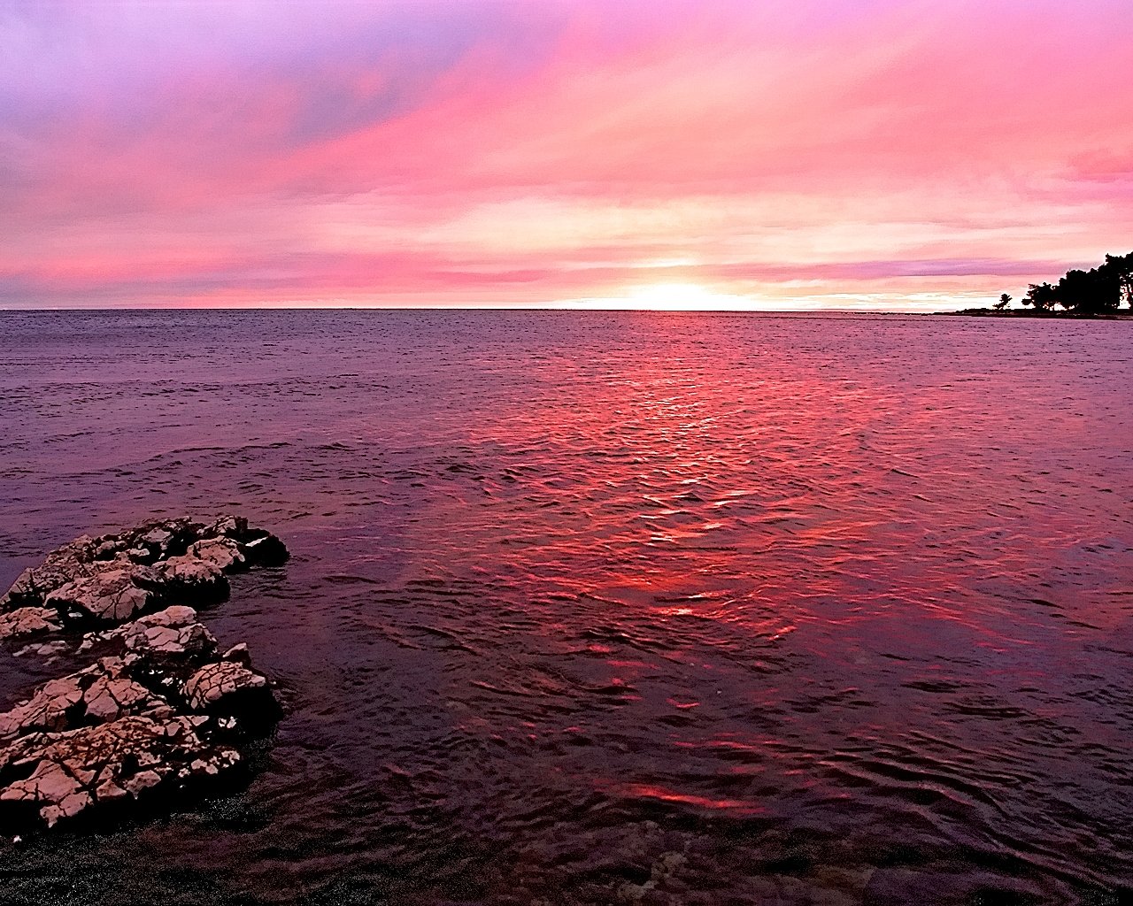 the sunset reflects on the water as a person stands on the rocks