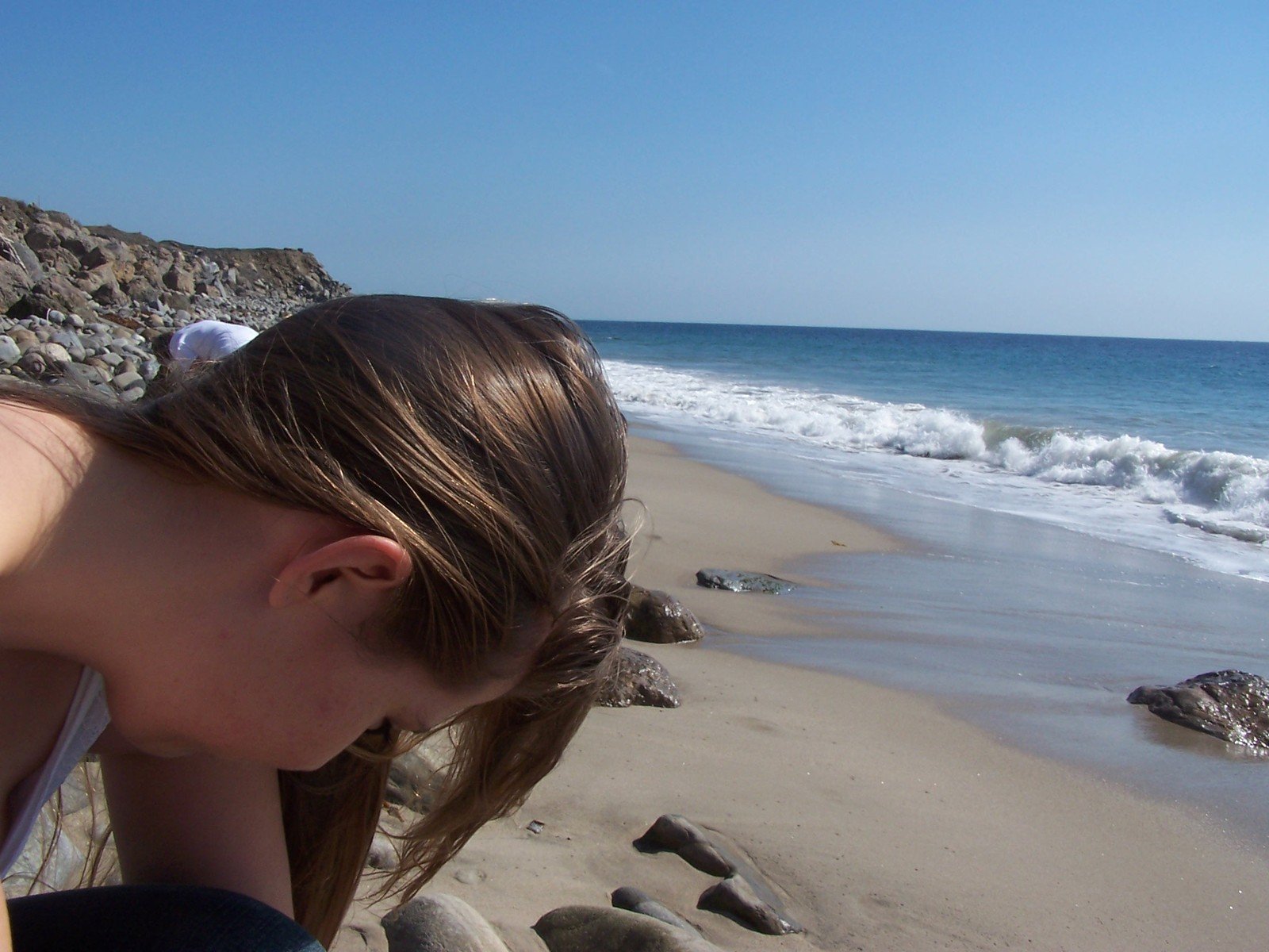 a woman stares off to the left with waves crashing in and behind her
