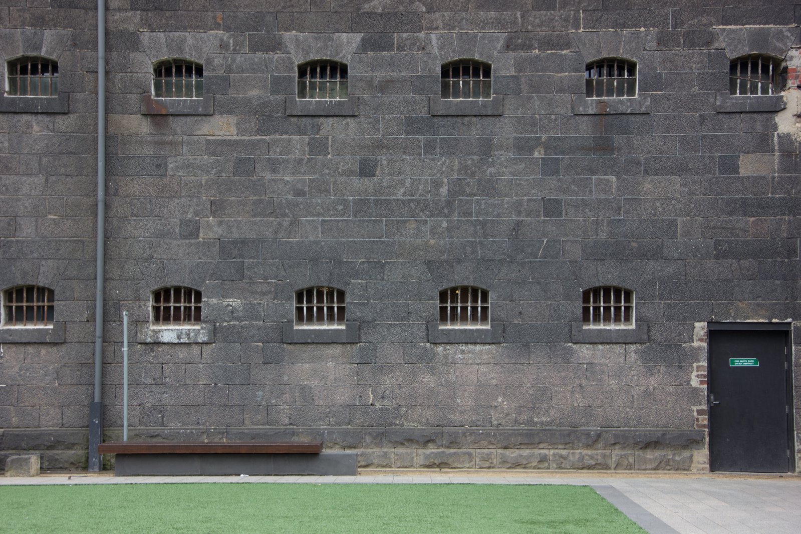 a wall made of grey brick with bars on one window and grass lawn in front