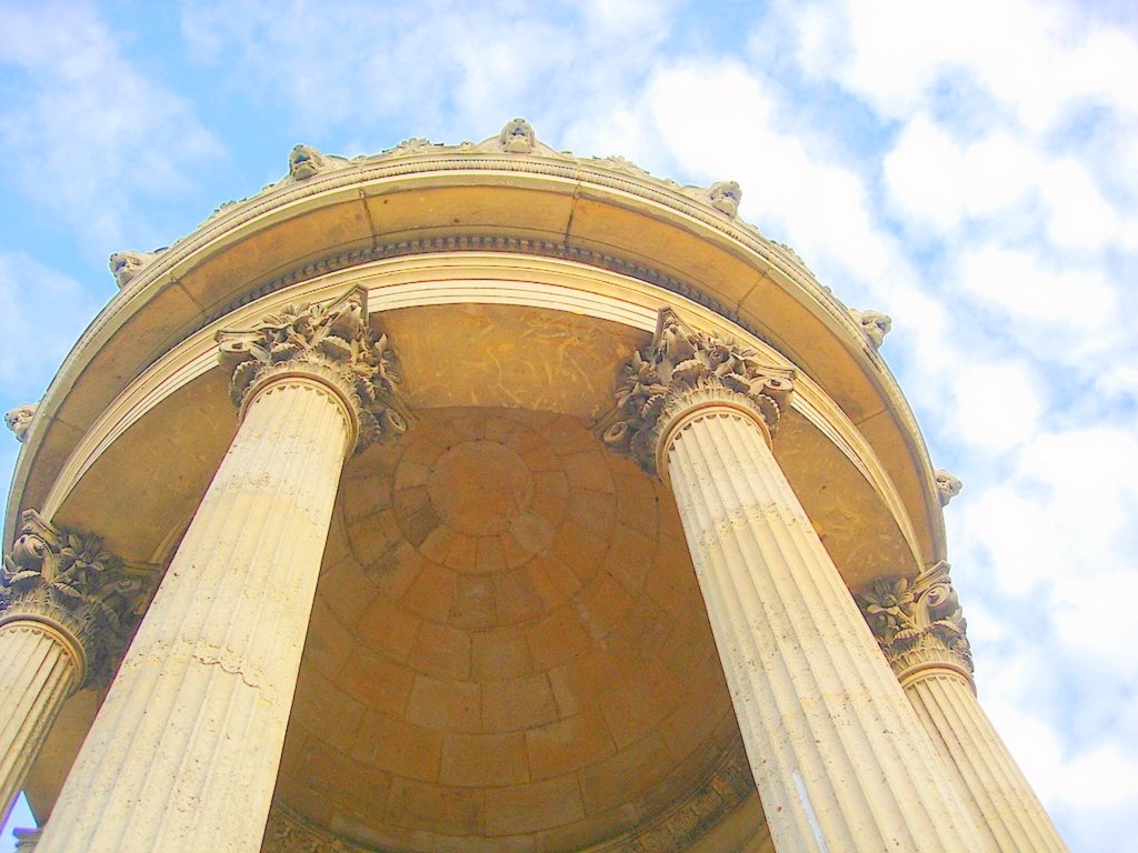 a tall building with four pillars under a cloudy sky