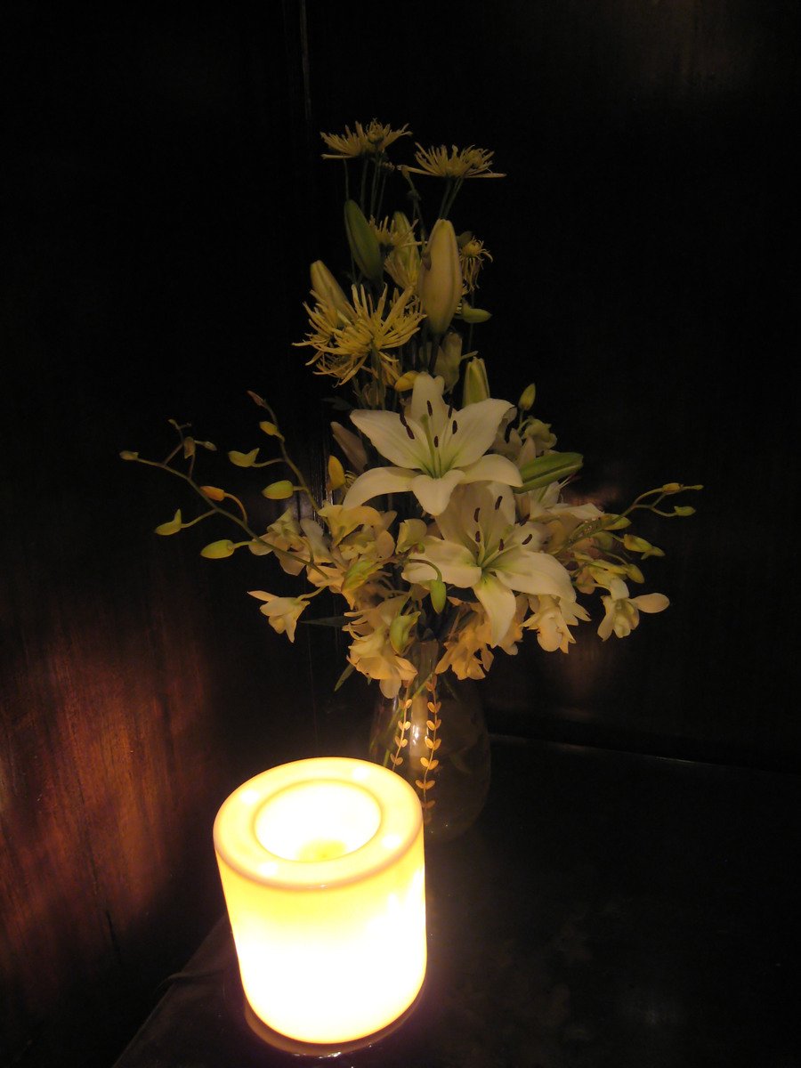 a glass vase with white flowers on the table next to a lit candle