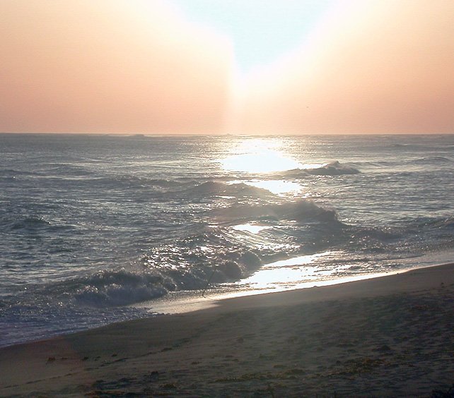 sun setting on an ocean with a beach and footprints in the sand