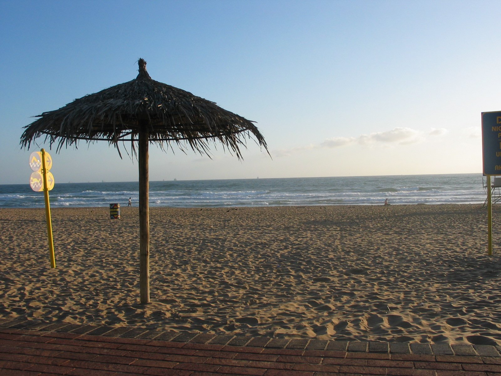 two thatch roofed umbrellas standing on top of a beach