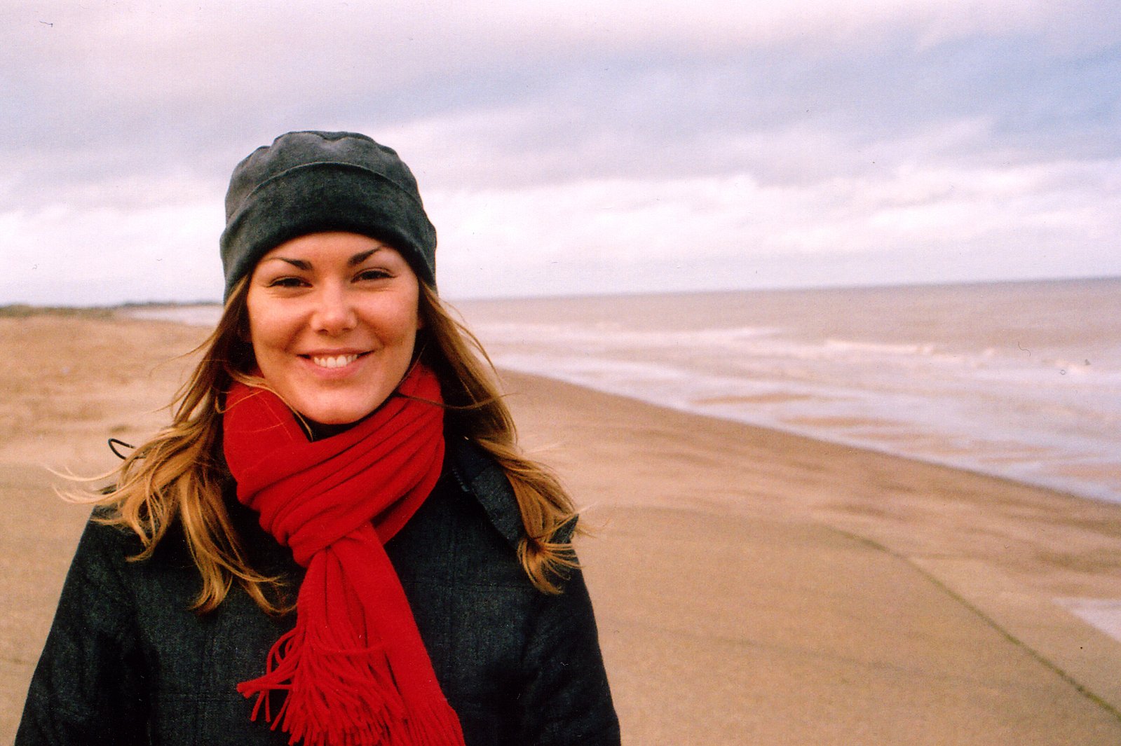 a woman smiles while wearing a black hat and red scarf