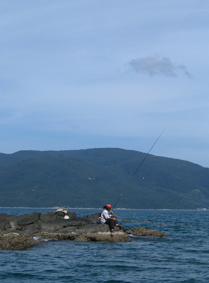 the man is fishing on the rocks with his pole