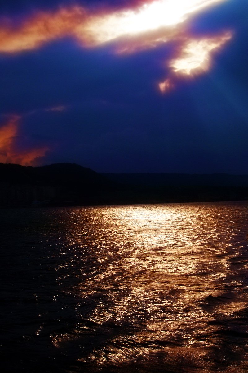 a water body with sun beams shining through the clouds