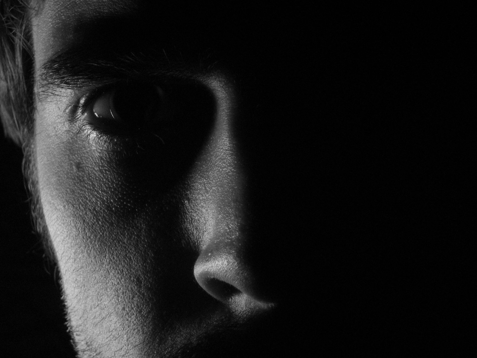 black and white pograph of man's face with left eye partially obscured by dark background