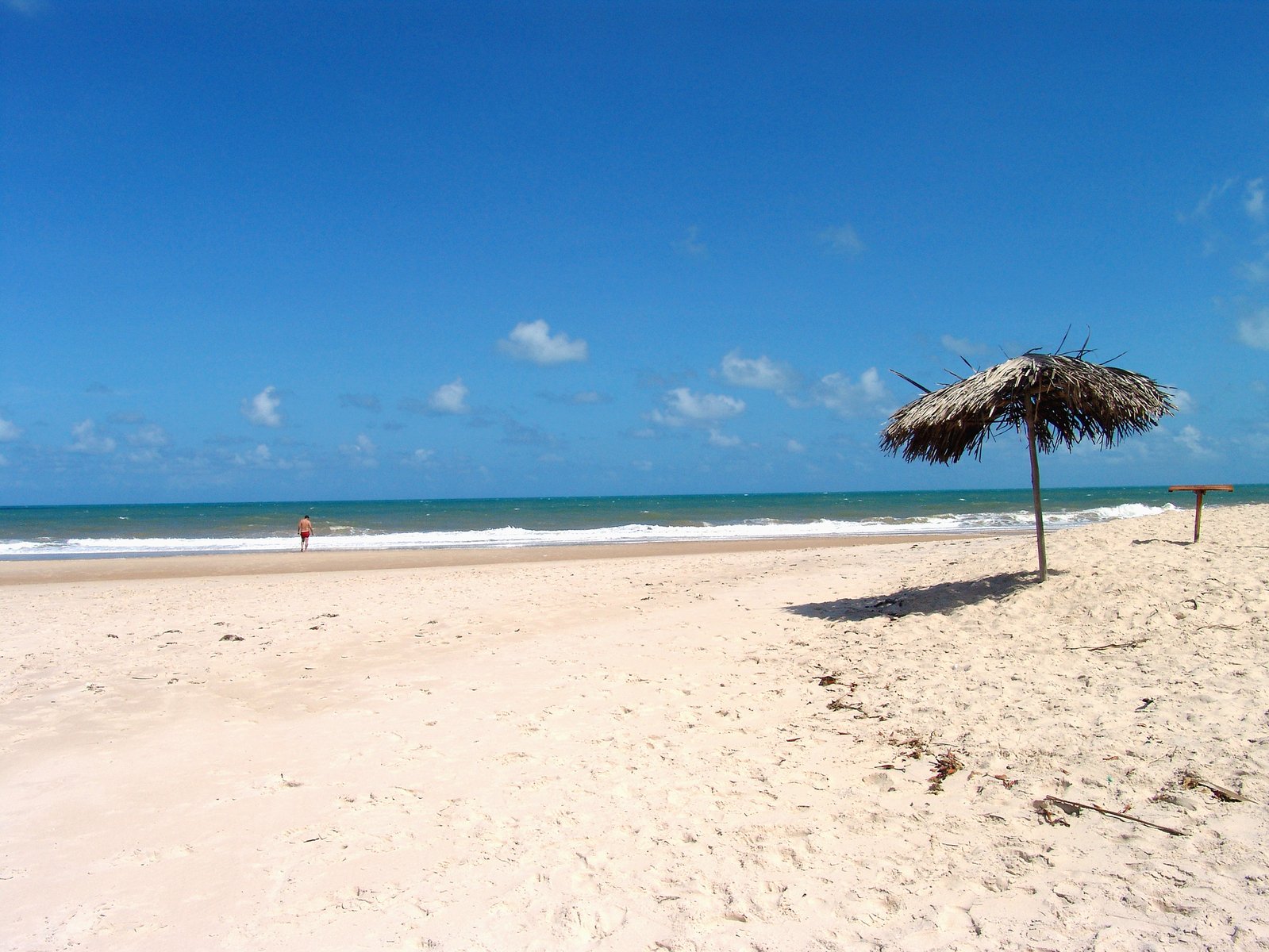 a lone beach umbrella sitting on the edge of a sandy shoreline