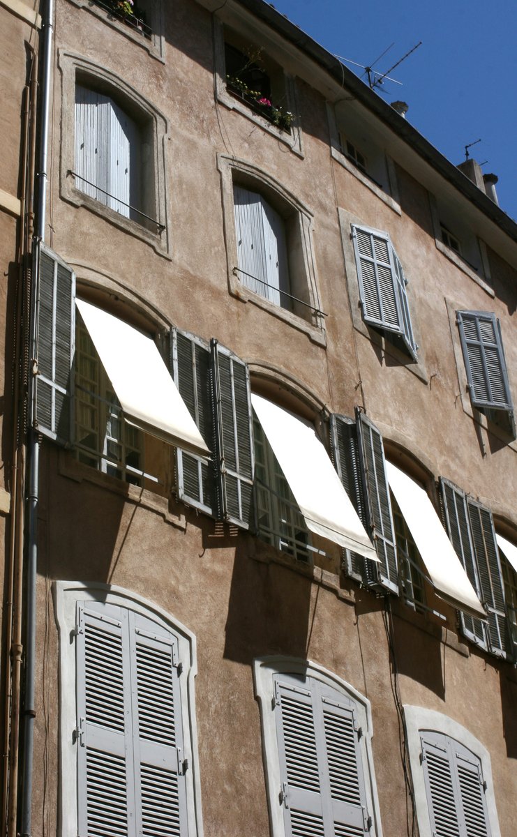 an old, stucco building with white window frames and shutters