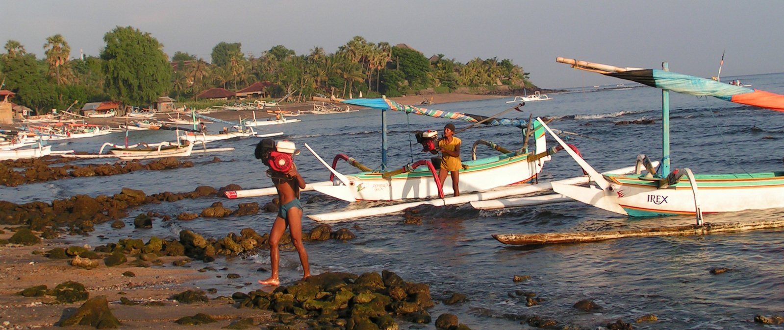 two woman in the ocean standing on the shore and pulling a small boat