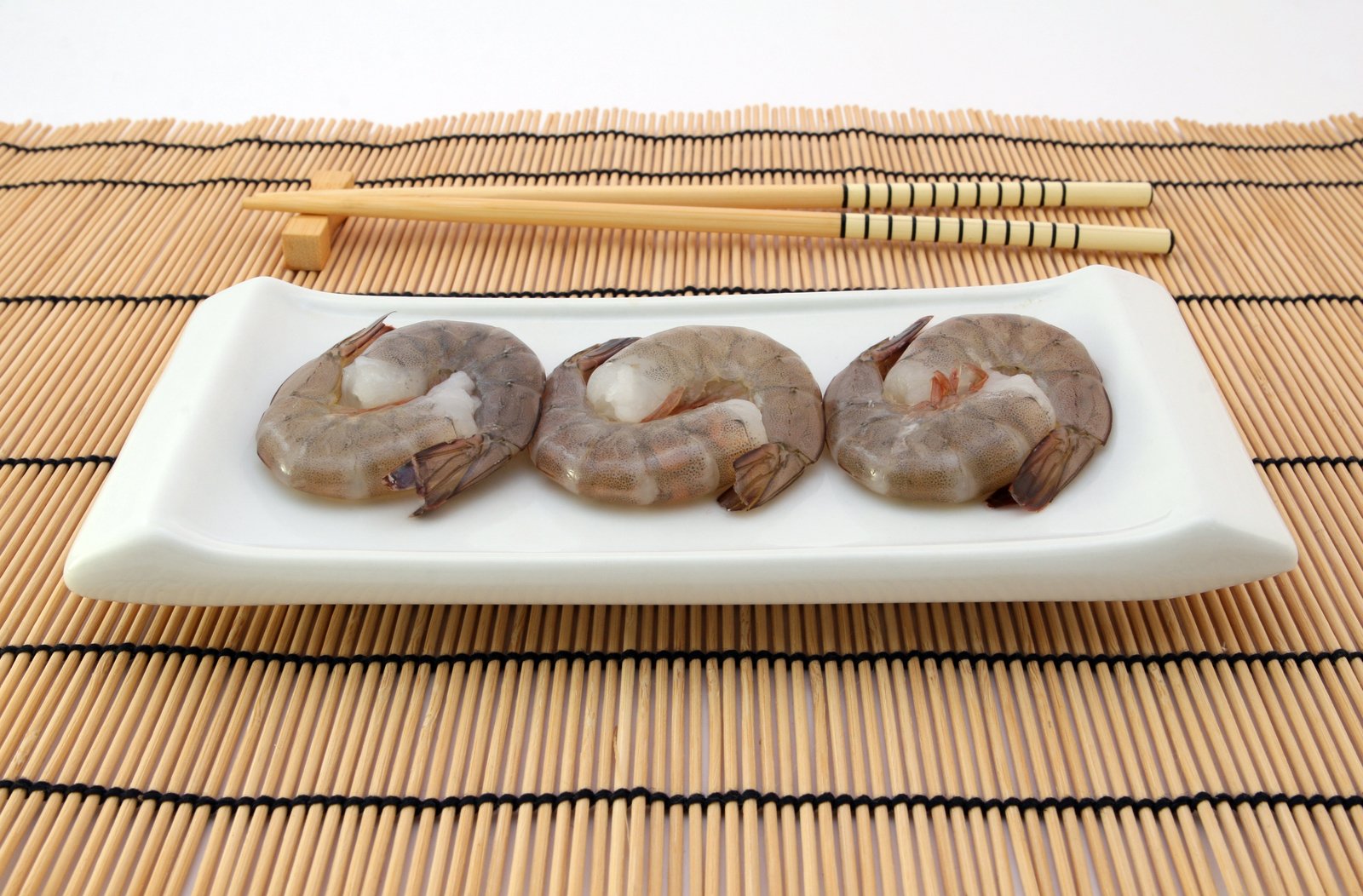 four raw, shrimp are on a white plate with chopsticks