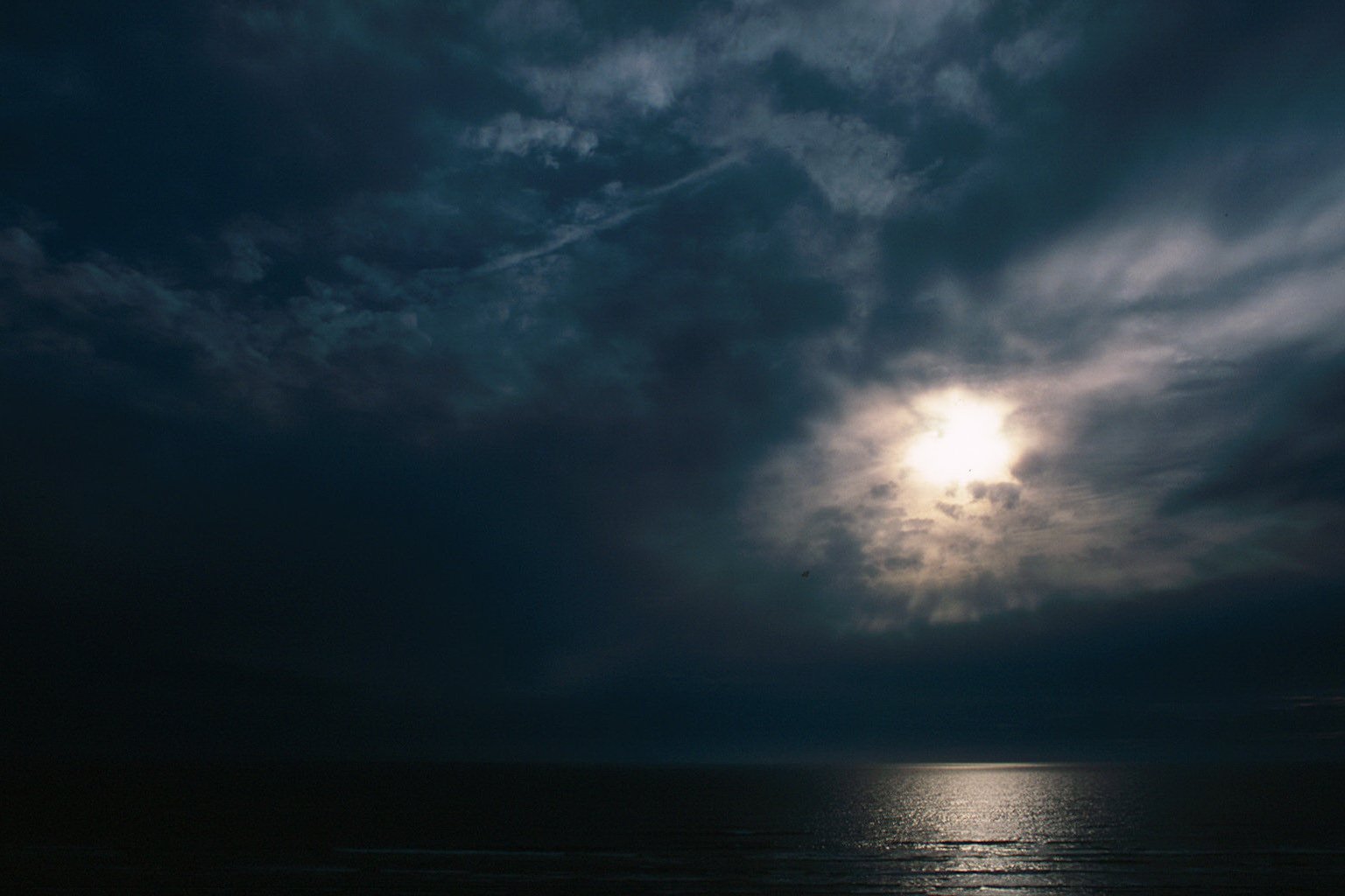 a boat sits under an approaching storm, with the sun shining through it