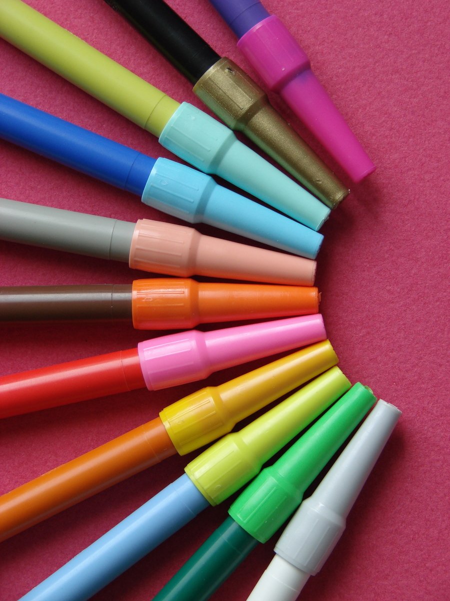 six different colored pens lined up on top of a pink surface