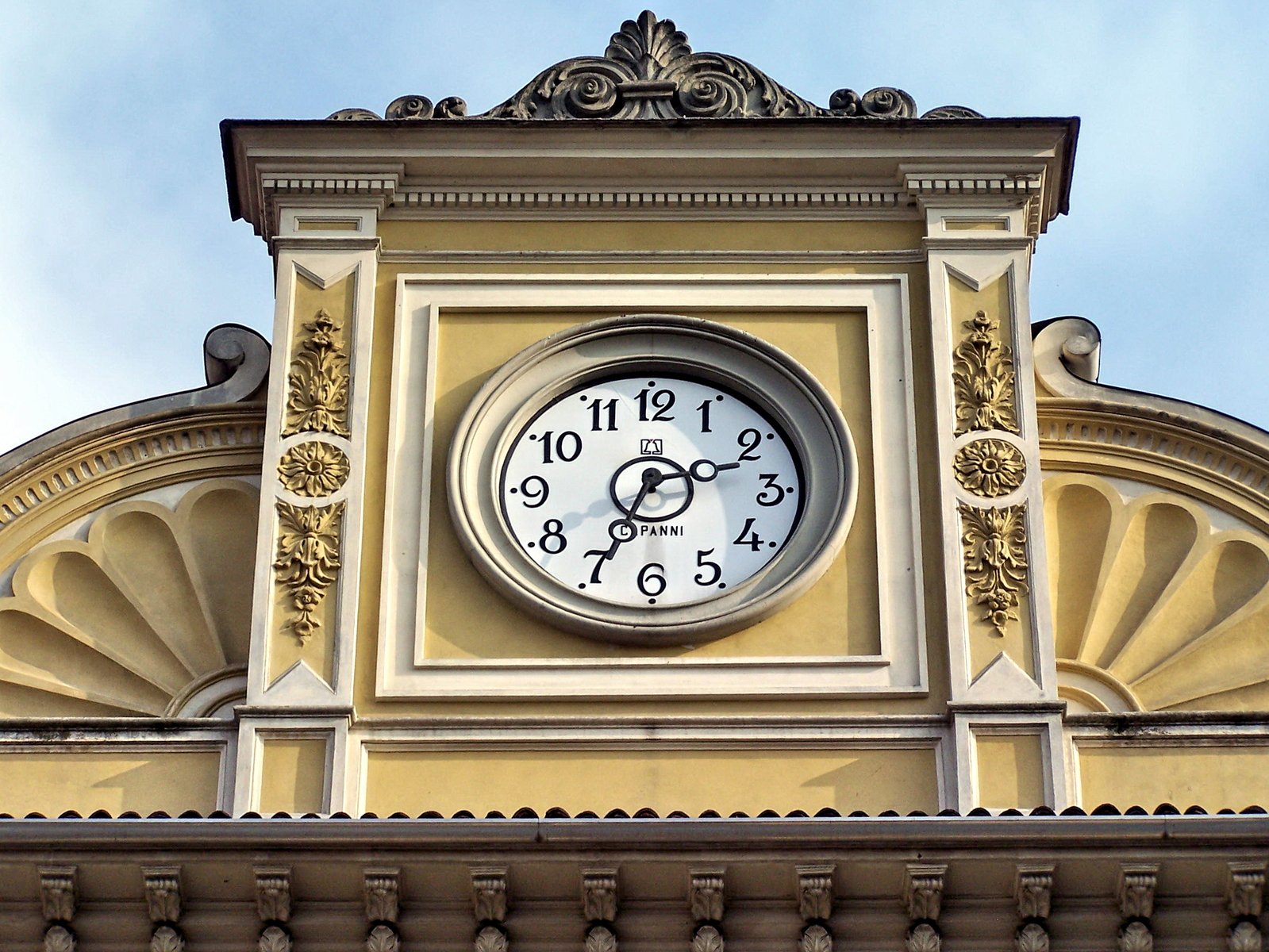 a large clock above a roof near many clouds
