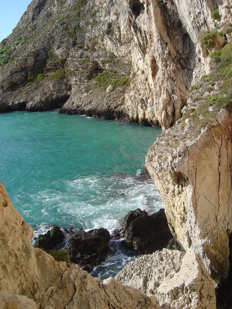 a rock cliff overlooking a body of water with a rock outcropping at the end