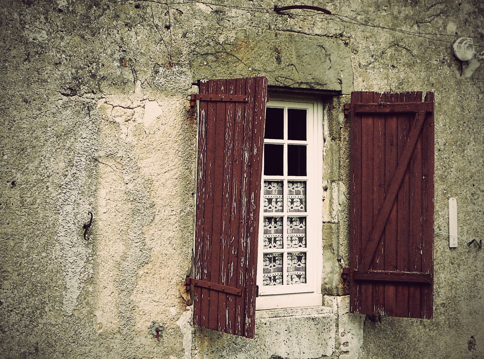 an old building with two brown shutters and one white window