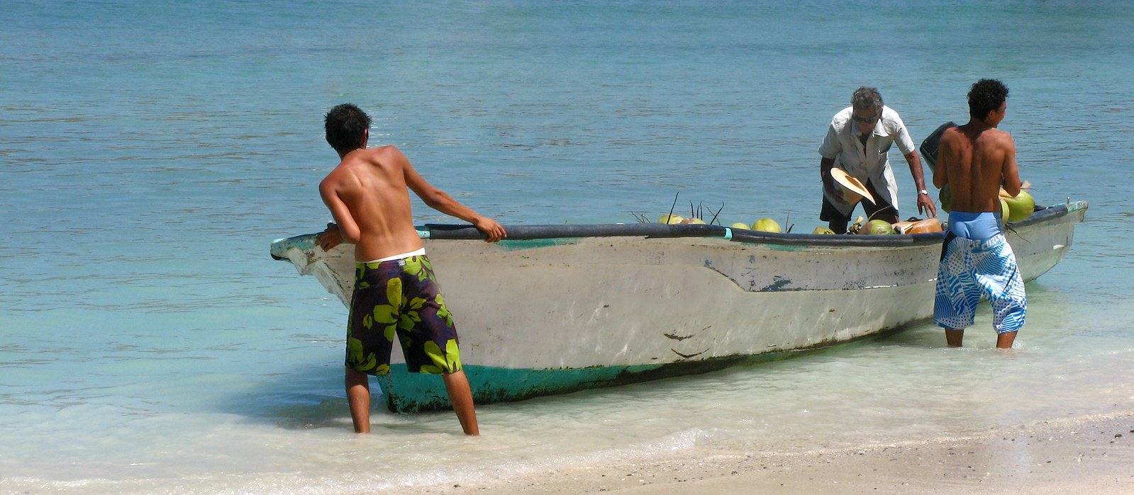 some men are standing in the shallow water by a boat