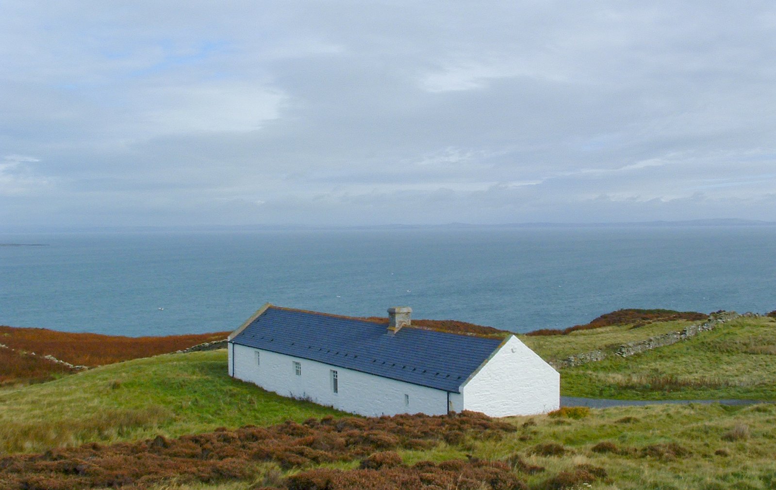 a white house is in the middle of a field near the ocean