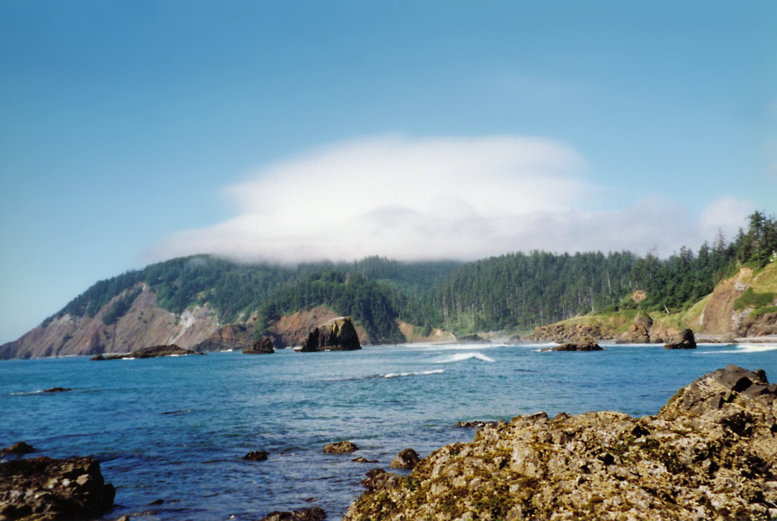 some large rocks a mountain a body of water and some trees