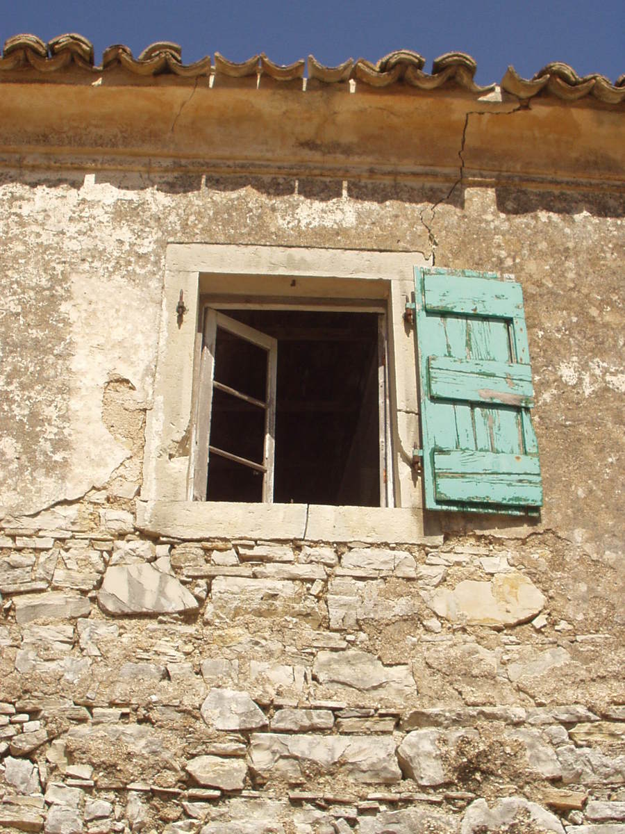 a weathered stone house has a wooden blue window