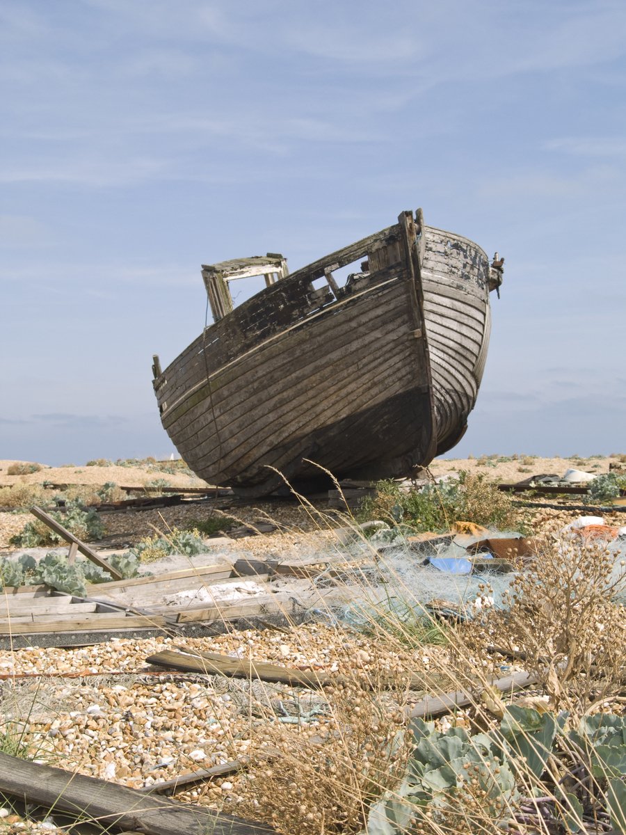 a wooden boat is laying on land next to dry grass