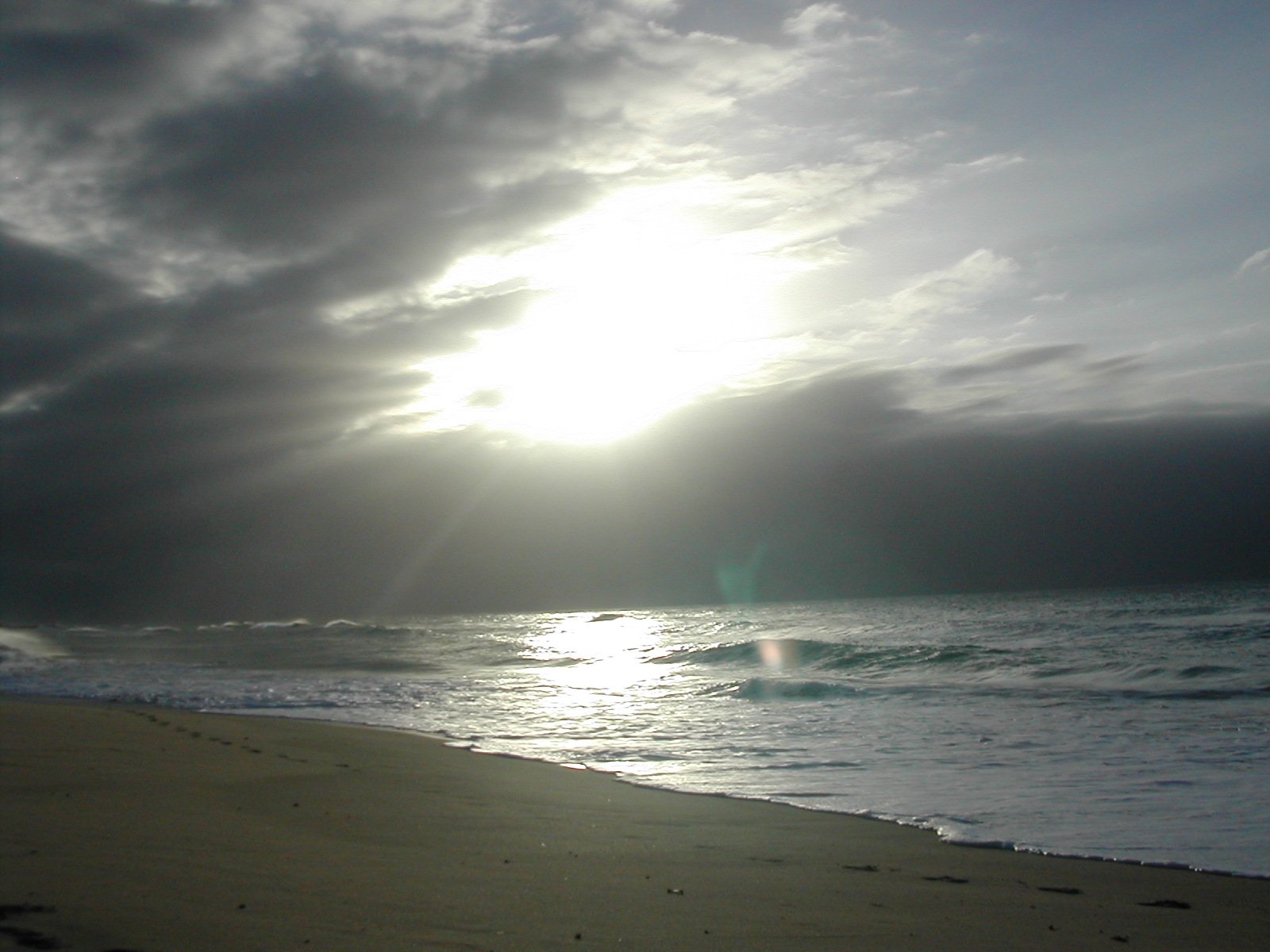 the sun shining through a cloudy sky next to a beach