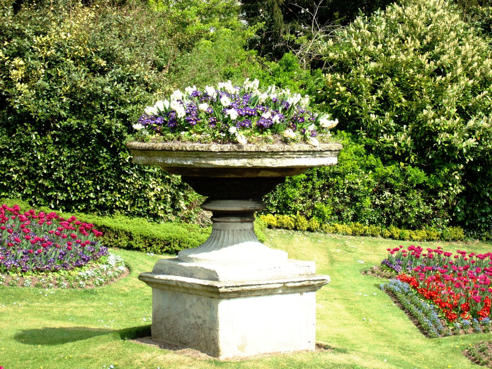 a circular planter sits in front of flowerbeds in a garden
