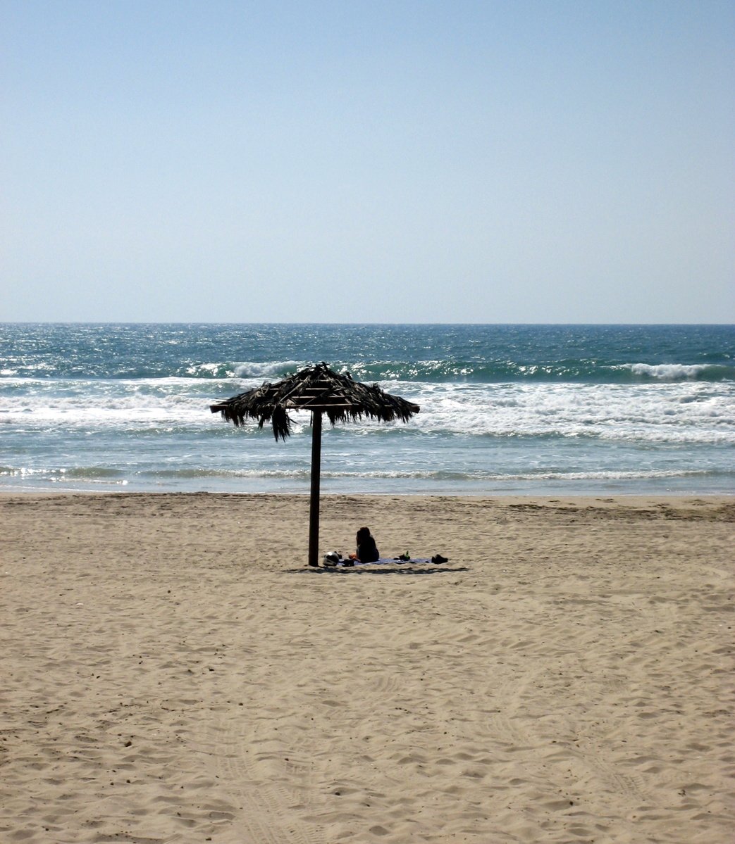 person sleeping under a wooden canopy on a beach