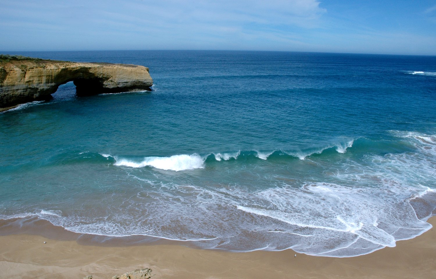 an arch shaped rock that extends into the ocean near a beach