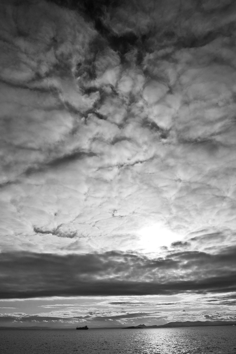 black and white image of clouds over water and a boat